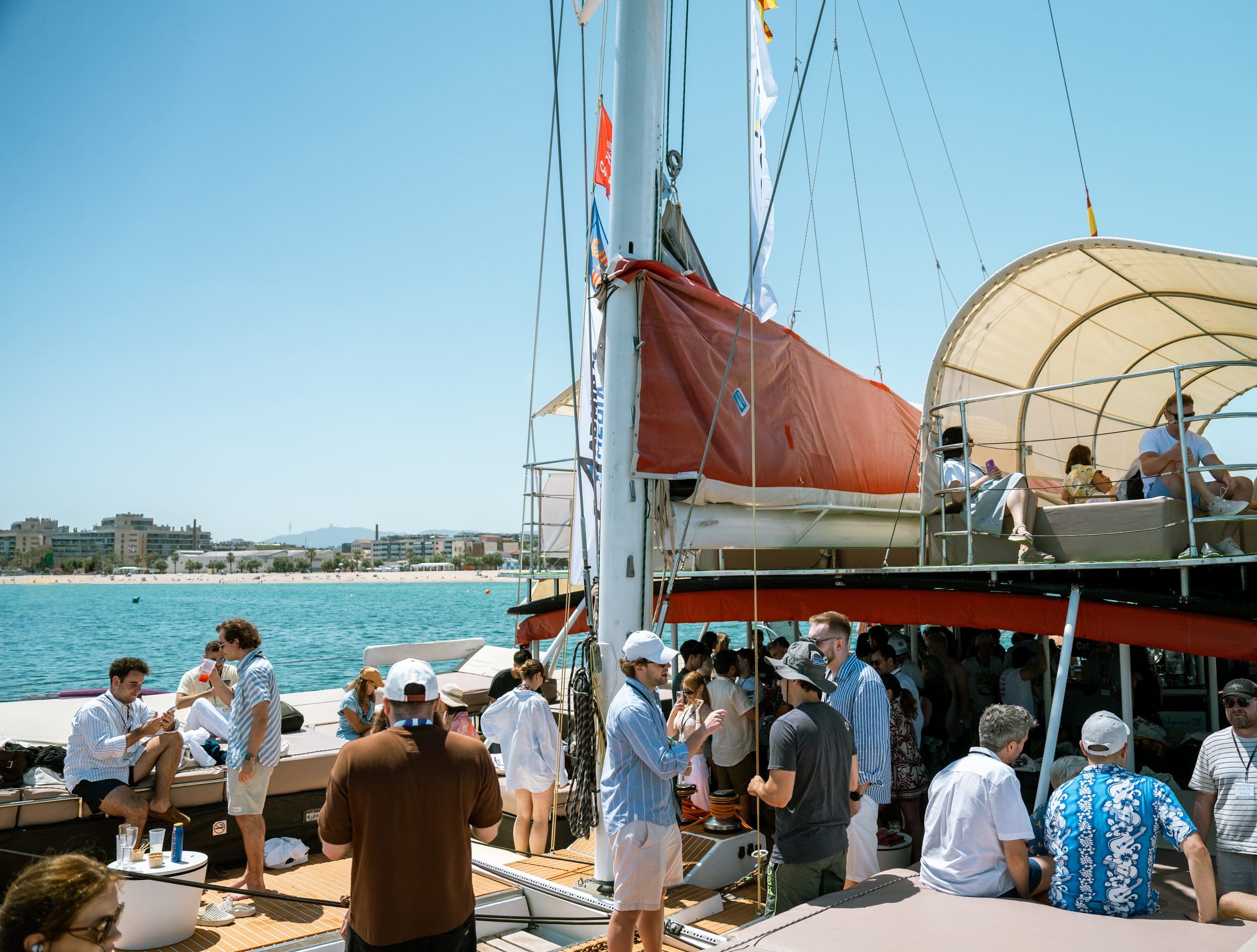 Wide view of the GrowBoat Barcelona catamaran with around 30 mobile growth leaders on deck and the Barcelona skyline behind in golden Mediterranean light