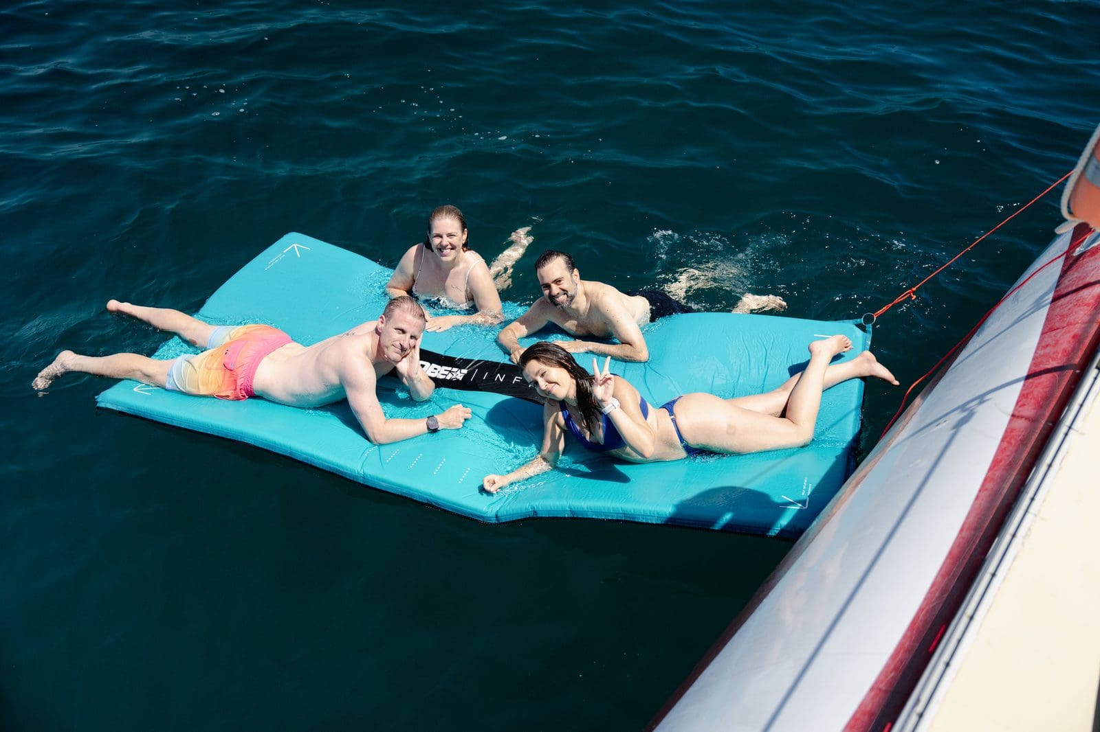 Four GrowBoat guests relaxing on a floating water mat in turquoise Mediterranean water beside the catamaran